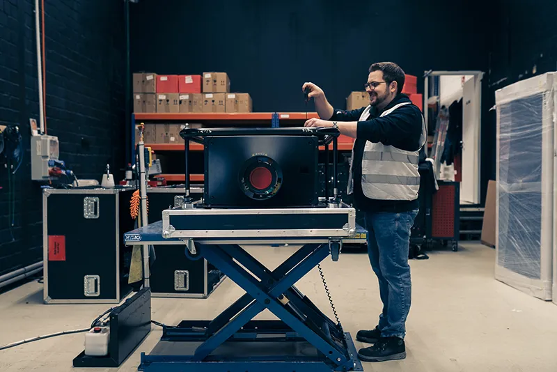 Techniker mit Weste schraubt an Projektor auf Hubtisch für Veranstaltungstechnik